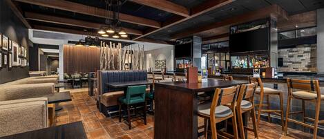 A modern bar area with wooden bar stools, a counter, and a seating area with cushioned benches and chairs.