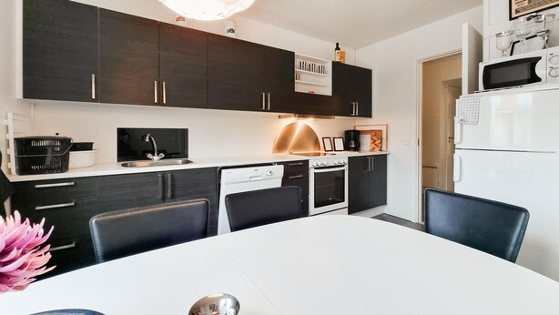 Una cocina moderna con armarios oscuros, una encimera blanca, un horno empotrado y un microondas.