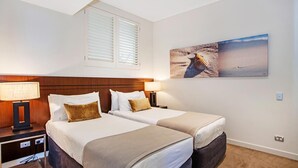 A hotel room with two beds, a wooden headboard, bedside lamps, and a beach-themed painting on the wall. - 1322 Luxury Beachfront Penthouse with Rooftop Jacuzzi (Kingscliff)