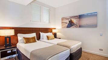 Une chambre d’hôtel avec deux lits, une tête de lit en bois, des lampes de chevet et un tableau sur le thème de la plage au mur.