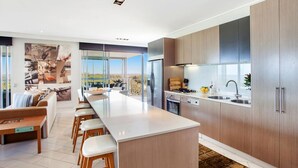 A modern kitchen with a central island, wooden cabinets, and a view of the outdoors. - 1322 Luxury Beachfront Penthouse with Rooftop Jacuzzi (Kingscliff)