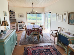 A dining area with a table, chairs, a chandelier, and a view through large windows.