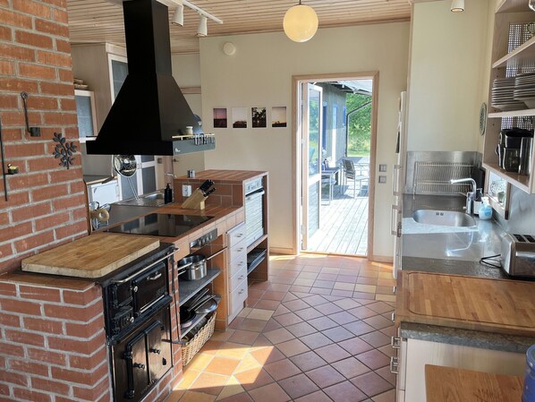 A modern kitchen with a brick wall, built-in ovens, a large island, and a view to an outdoor deck.