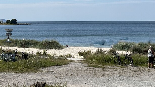 Una playa con un cartel, bicicletas y un camino que lleva al agua.