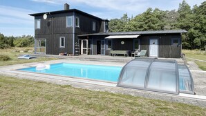 Una casa moderna de dos pisos con piscina, mobiliario exterior y un patio cubierto.