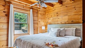 Une chambre dans une cabane en bois, avec un lit, un ventilateur de plafond et une fenêtre avec des rideaux.