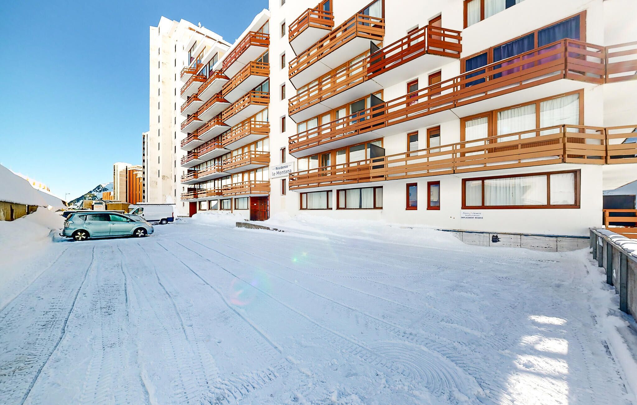 Un hotel de varios pisos con balcones de madera, una calle cubierta de nieve y un cielo despejado.