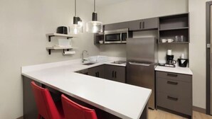 Een moderne keuken met een centraal eiland, rode stoelen, roestvrijstalen apparatuur en hanglampen.
