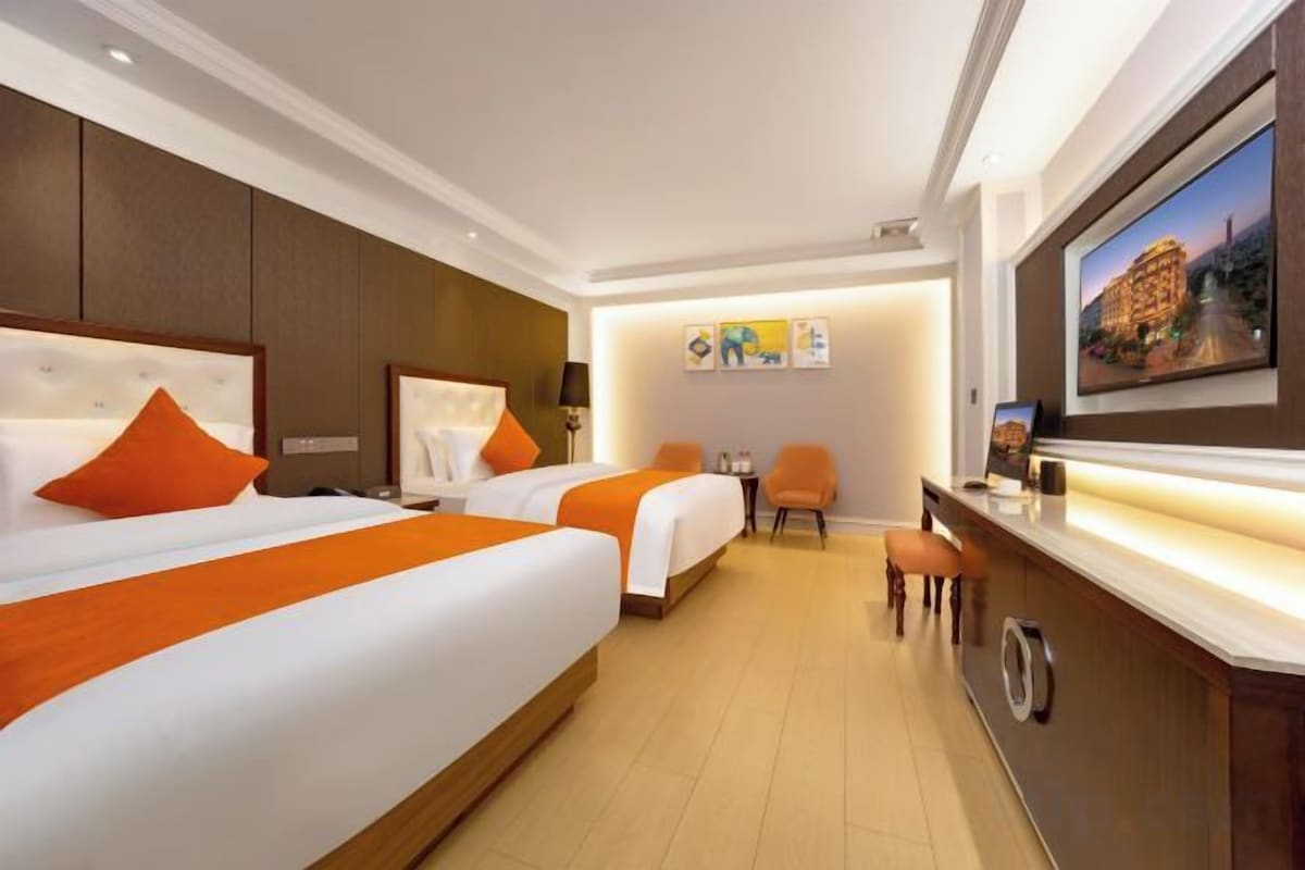 A hotel room with two beds, a desk, and a television.