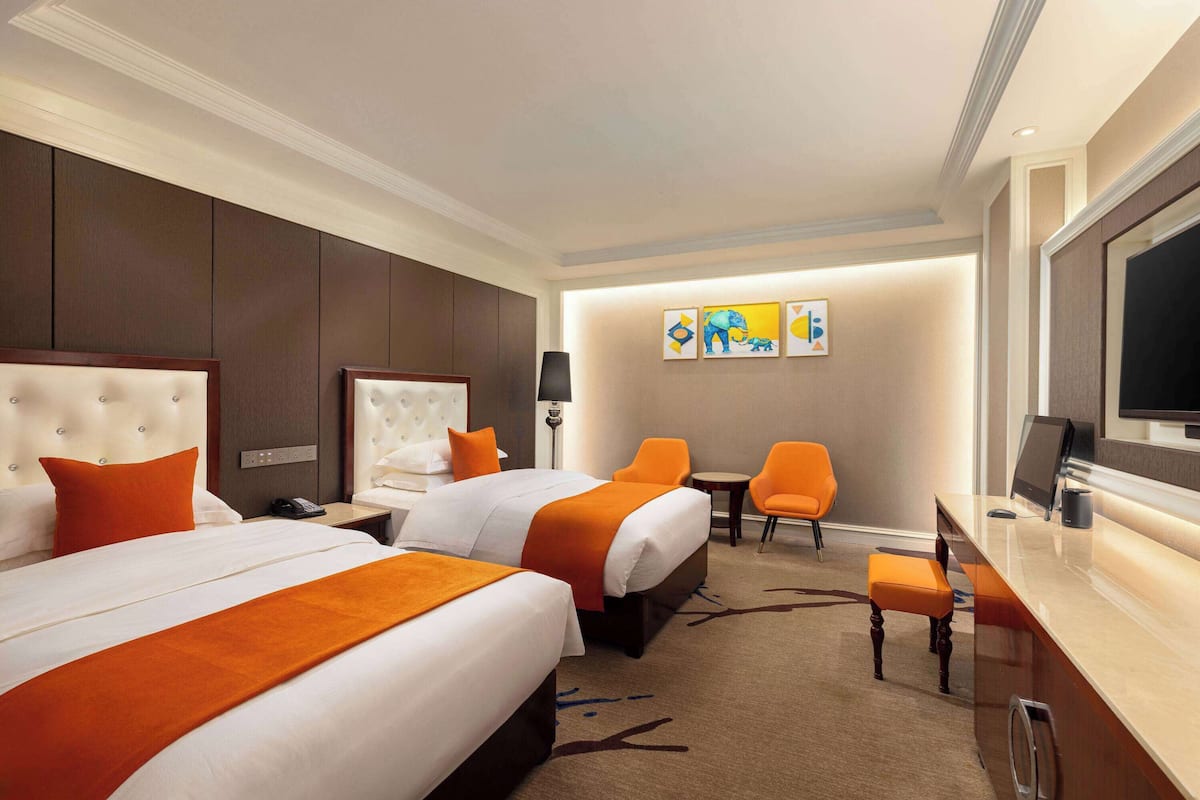 Ein Hotelzimmer mit zwei Betten, einem Schreibtisch, einem Stuhl und Bildern an der Wand.