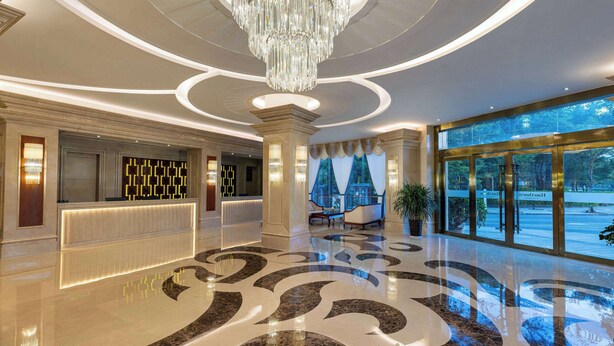 A hotel lobby with a grand chandelier, a reception desk, and large windows offering a view of the outdoors.