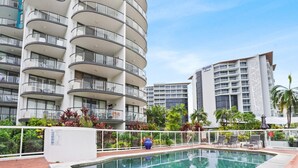 A modern hotel with a pool area, featuring a multi-story building with balconies, a swimming pool, and tropical landscaping. - Charming 1-Bedroom Apartment with Rooftop Pool & Prime Cairns Location (Cairns City)