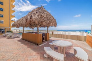 Une terrasse au bord de la plage, dotée d’une structure à toit de chaume, de sièges extérieurs et offrant une vue sur l’océan.