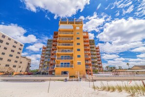 Un hôtel à plusieurs étages doté de balcons, avec une plage au premier plan et des palmiers en arrière-plan.