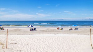 Une plage de sable blanc, un ciel bleu clair et une mer calme. On y trouve des parasols et des gens qui se détendent.
