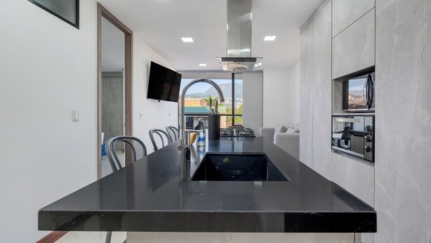 A modern kitchen with a central island, a built-in stove, and a large window offering a view of the outdoors.
