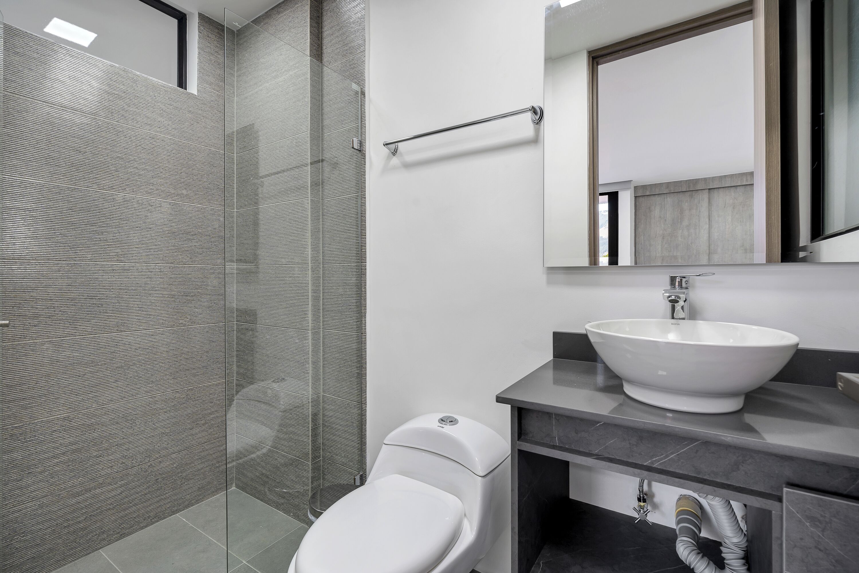 Een moderne badkamer met een douchecabine van glas, een wit toilet en een groot wastafelmeubel met spiegel.