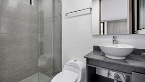 A modern bathroom with a glass shower enclosure, a white toilet, and a large sink with a mirror above it.