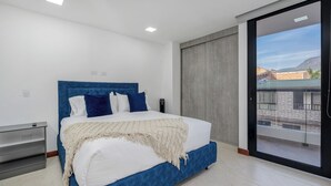 A modern bedroom with a large bed, a nightstand, and a sliding glass door to a balcony.