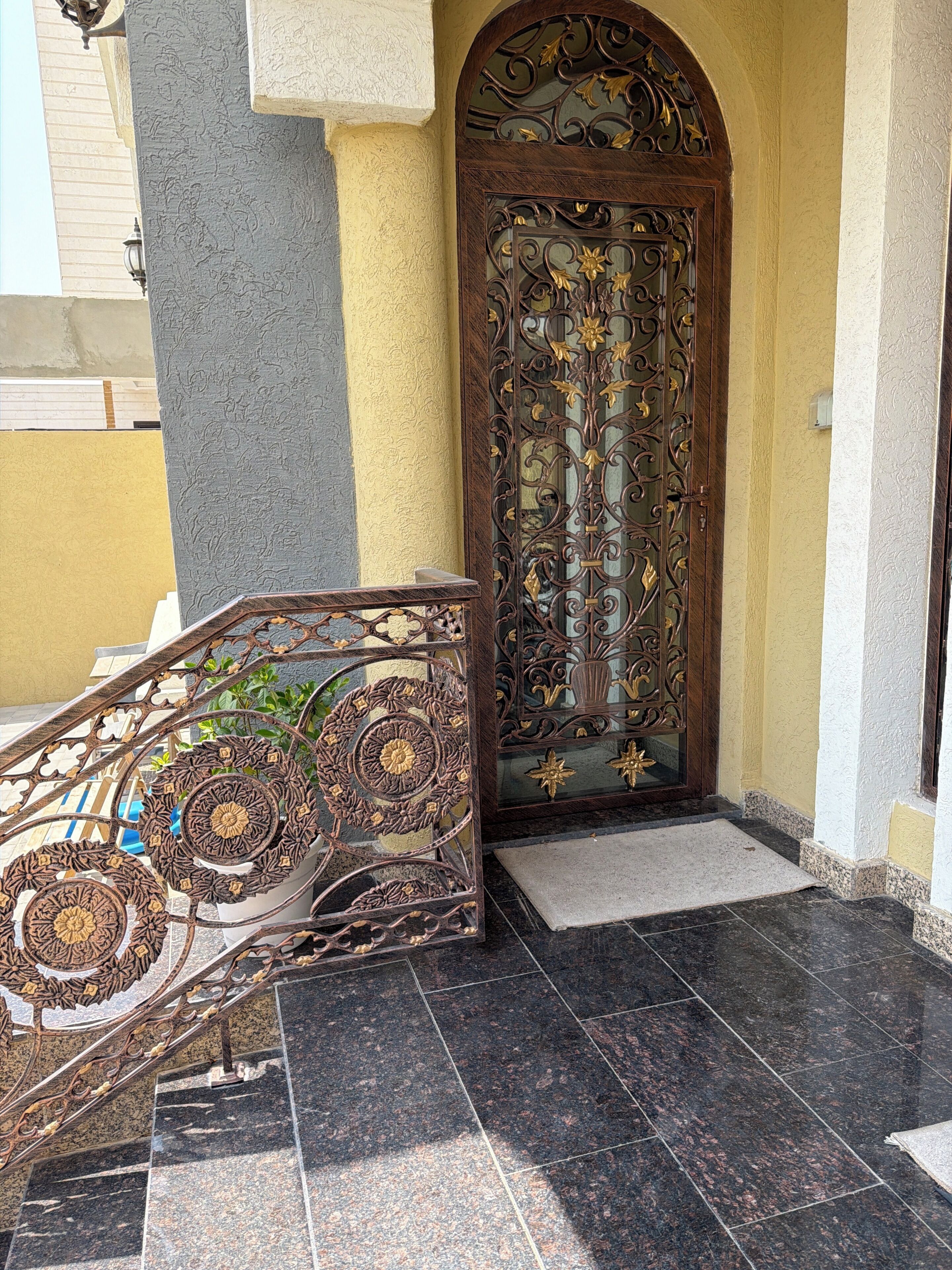 Una escalera con barandillas metálicas ornamentadas que conduce a una puerta con diseños intrincados.