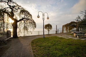 A paved walkway with benches, a lamppost, and a tree-lined path by a body of water. - [Verbania-Suna] Liebesnest Apartment - 50 meters from the lake - Free Wi-Fi (Verbania)