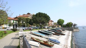 A waterfront promenade with boats docked along the shore, a pathway, and buildings in the background. - [Verbania-Suna] Love Nest Apartment - 50m from the lake - Free Wi-Fi (Verbania)