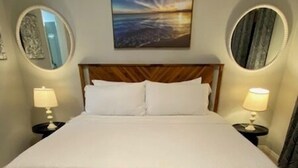 Una cama bien hecha con ropa de cama blanca, cabecera de madera y un banco en frente. Hay dos lámparas de noche y dos espejos montados en la pared.
