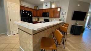Una cocina con encimera de mármol, armarios de madera, un refrigerador negro, un microondas y un reloj en la pared.