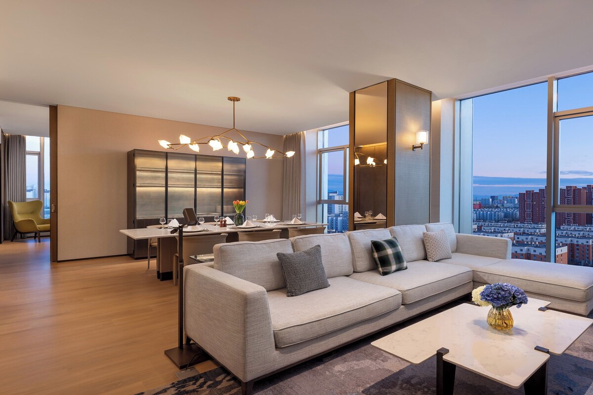 A modern living room with a large sofa, dining area, and large windows offering city views.