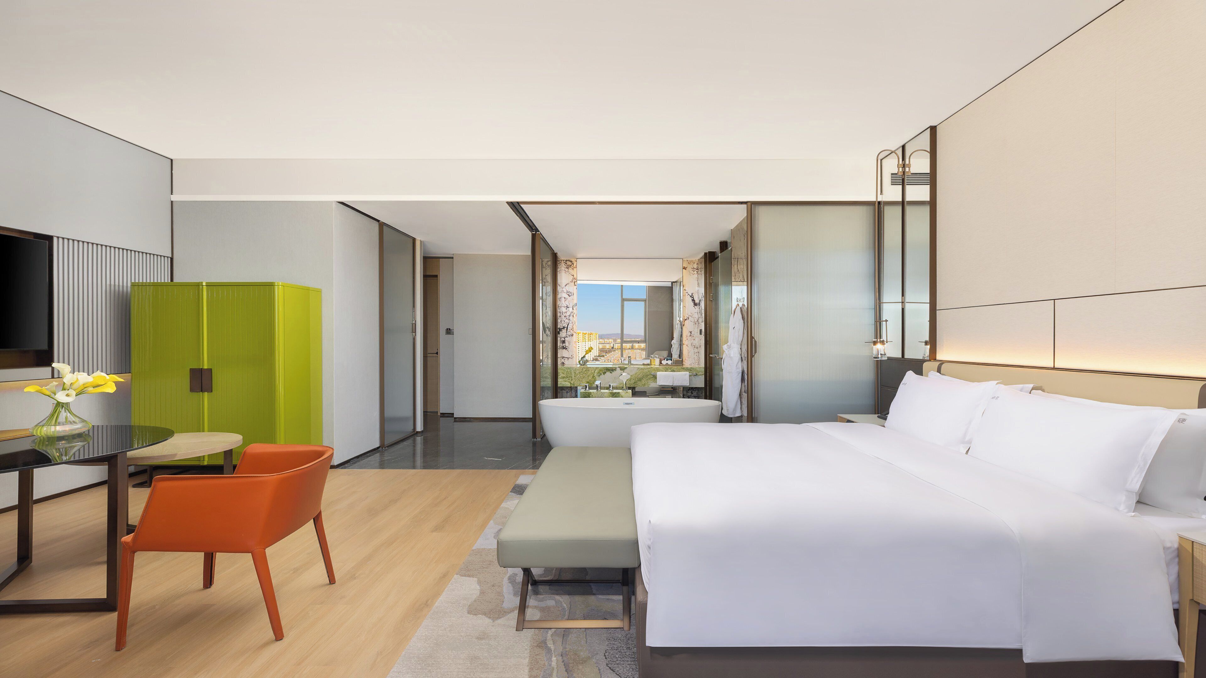 Una habitación de hotel moderna con una cama grande, un escritorio con silla, un mueble verde y vistas a la ciudad.