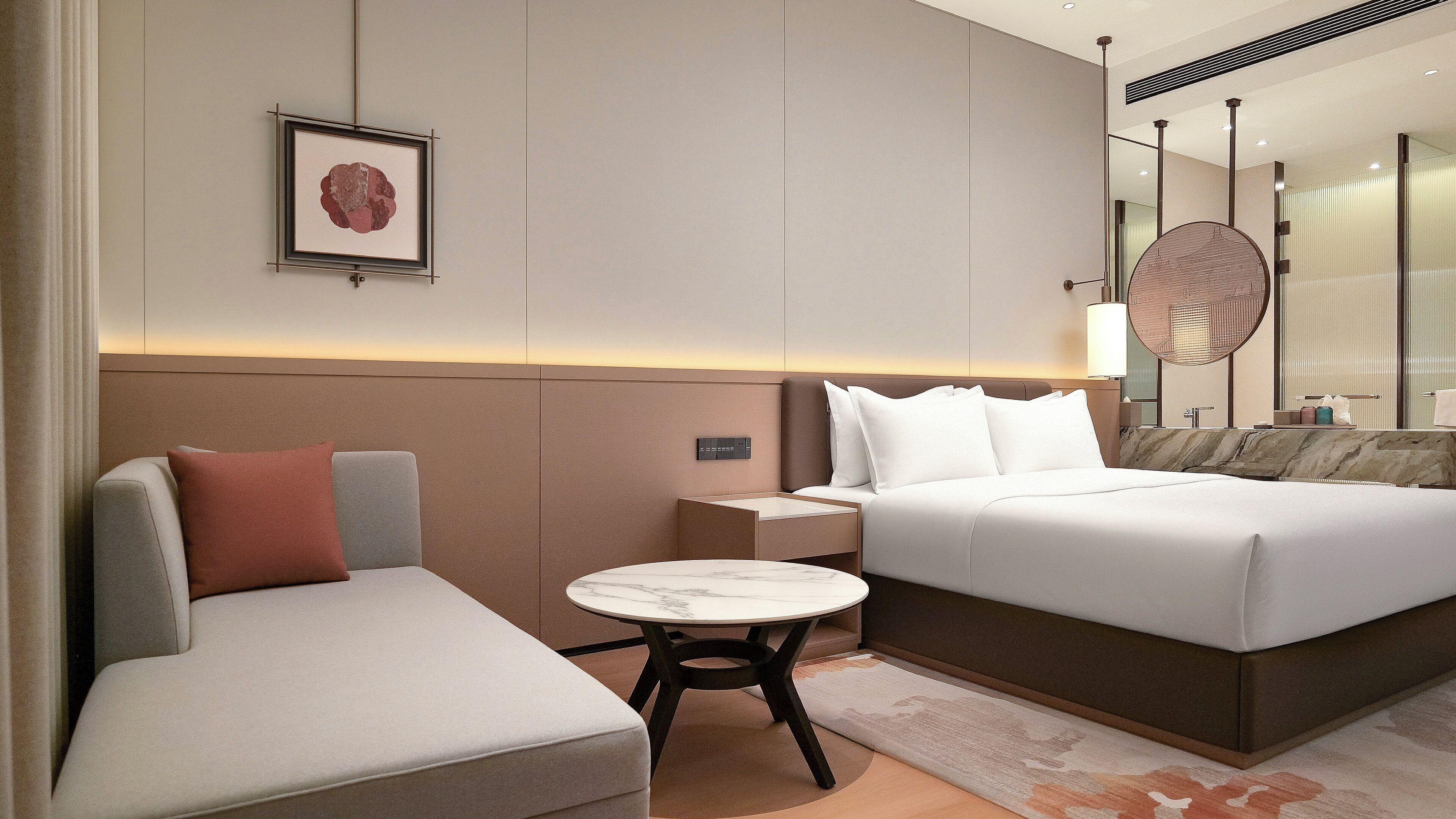 A modern hotel room with a bed, a sofa, a small table, and a bedside table.
