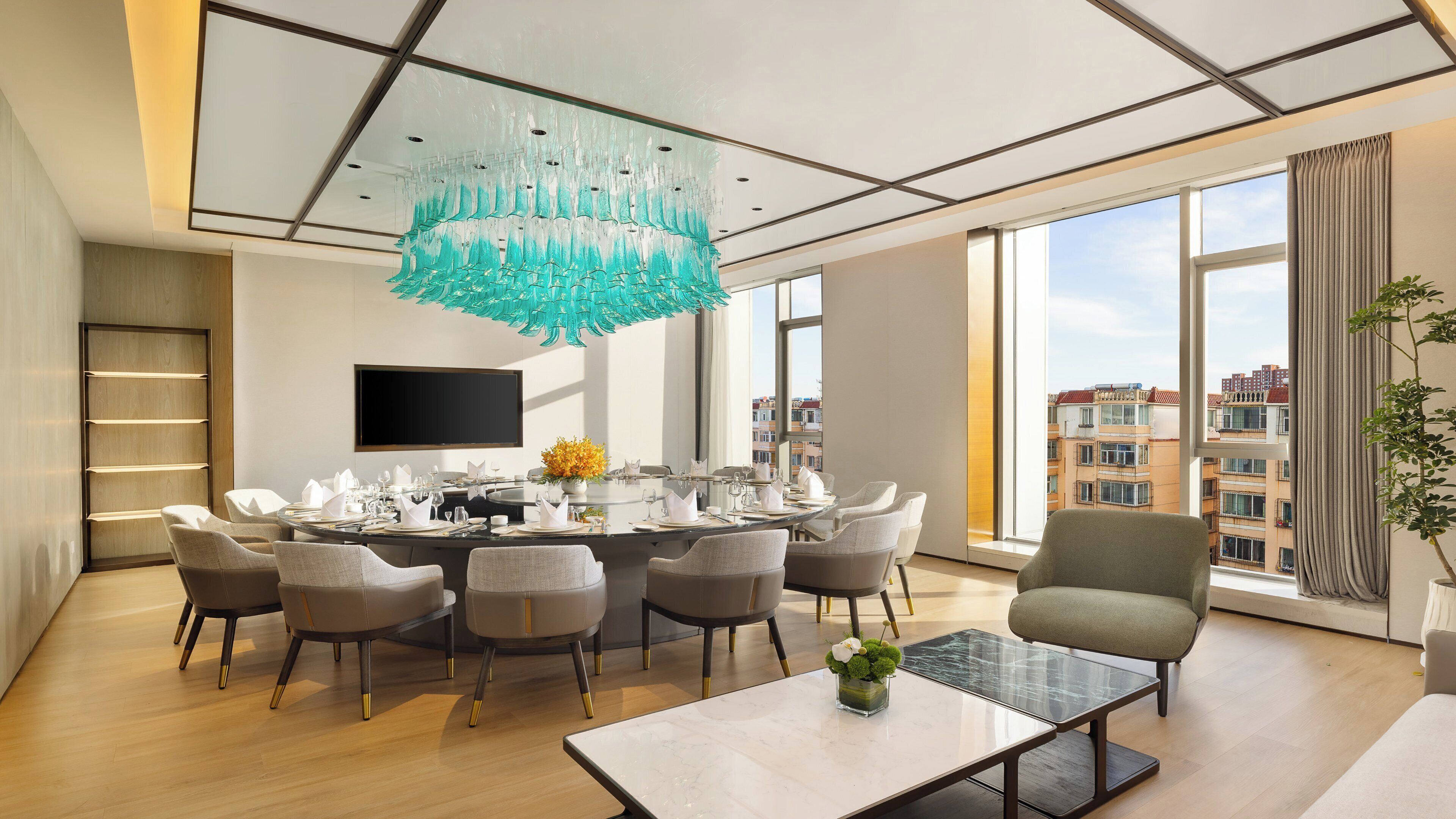 Un comedor moderno con una mesa redonda dispuesta para seis comensales, un ventanal con vistas a la ciudad y una lámpara colgante de color turquesa original.