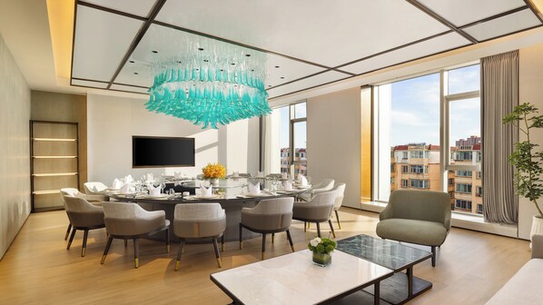 A modern dining room with a round table set for six, a large window with a city view, and a unique teal chandelier. - Holiday Inn Datong by IHG (Datong)