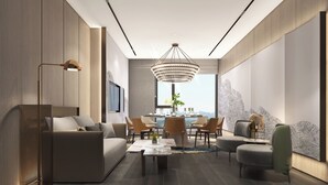 A modern living room with a sofa, coffee table, and chairs, a dining area with a chandelier, and a large window offering a city view.