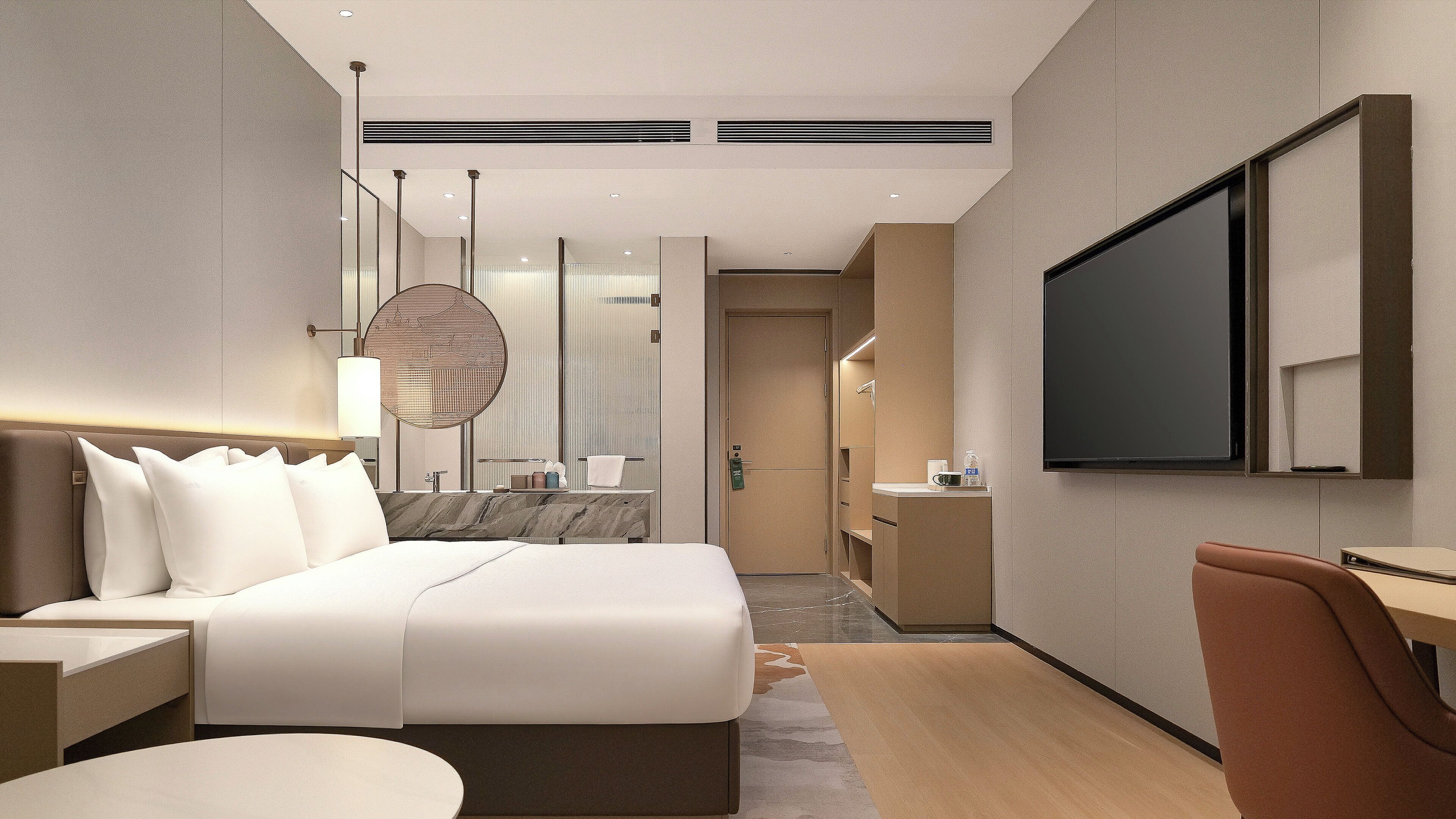 Ein modernes Hotelzimmer mit einem großen Bett, einem Fernseher, einem Schreibtisch und einem durch eine Tür erreichbaren Badezimmer.