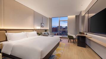 Habitación de hotel moderna con una cama grande, un escritorio, una silla y un amplio ventanal con vistas a la ciudad.
