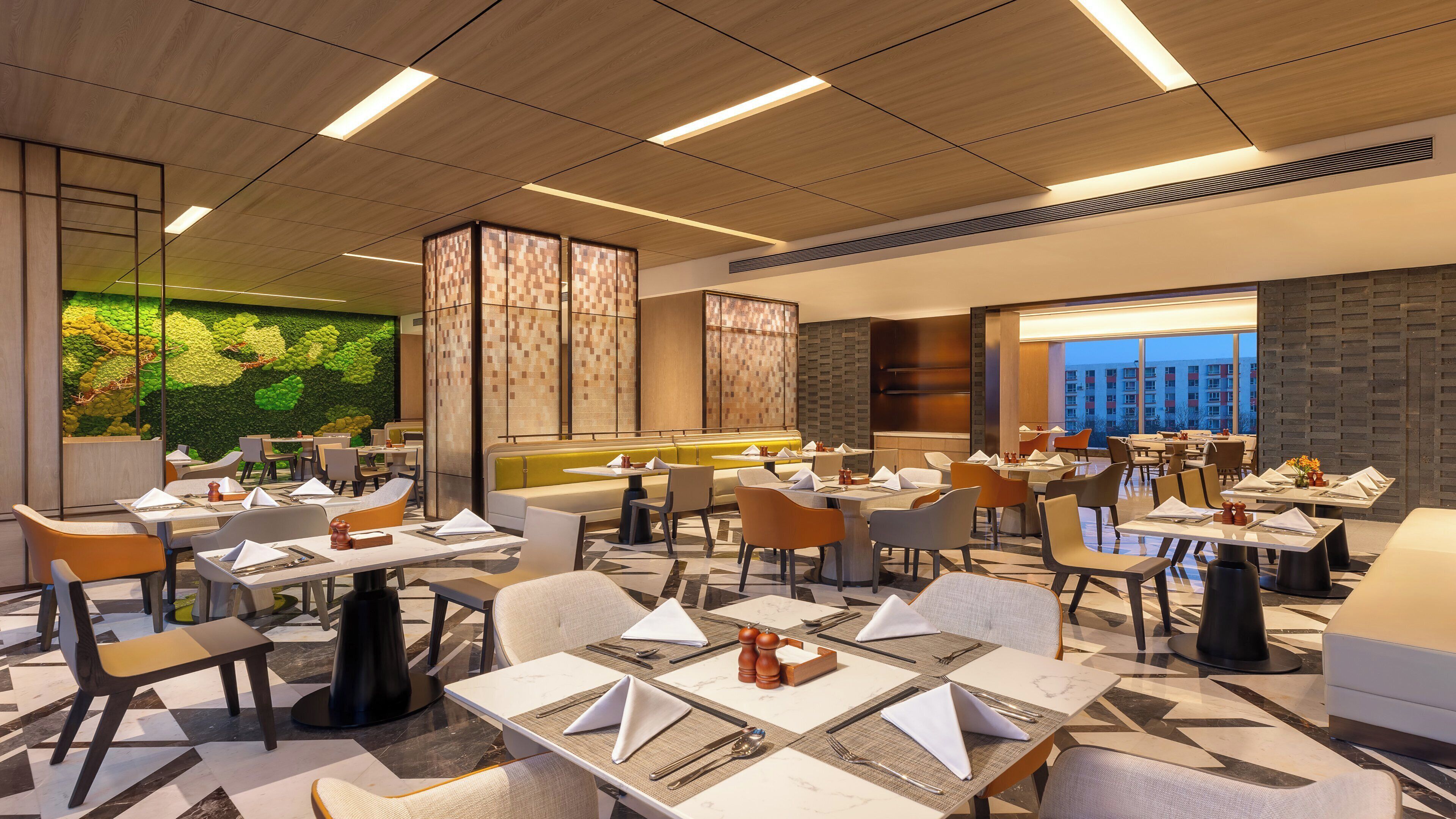 Um restaurante moderno com várias áreas de refeição, incluindo cabines e mesas, e uma parede verde com design natural.