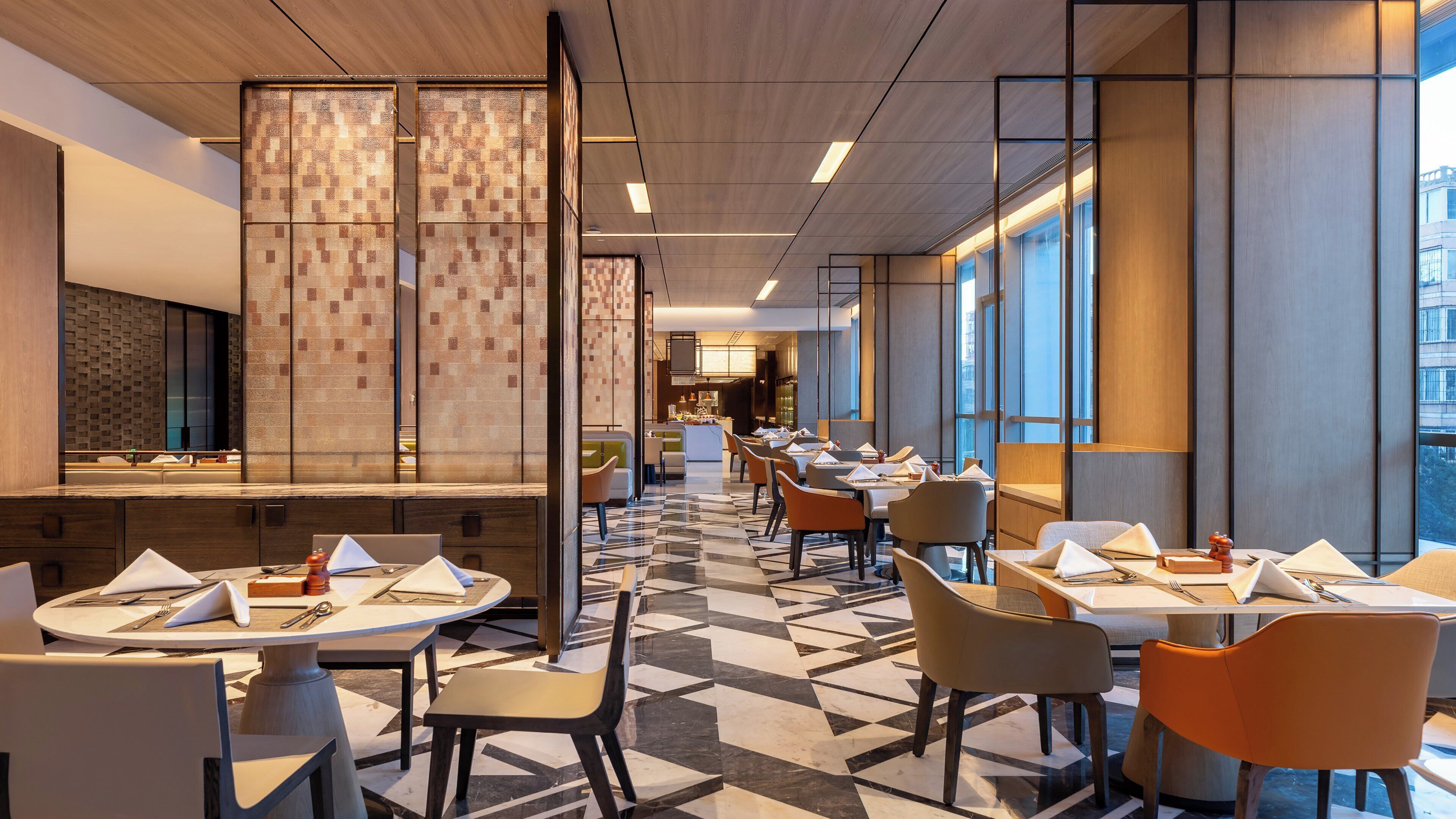 Un restaurante moderno con suelo de baldosas geométricas, paneles de madera y vistas a la ciudad a través de amplios ventanales.