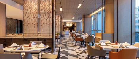 A modern restaurant with a geometric tile floor, wooden panel walls, and a view of the city through large windows.