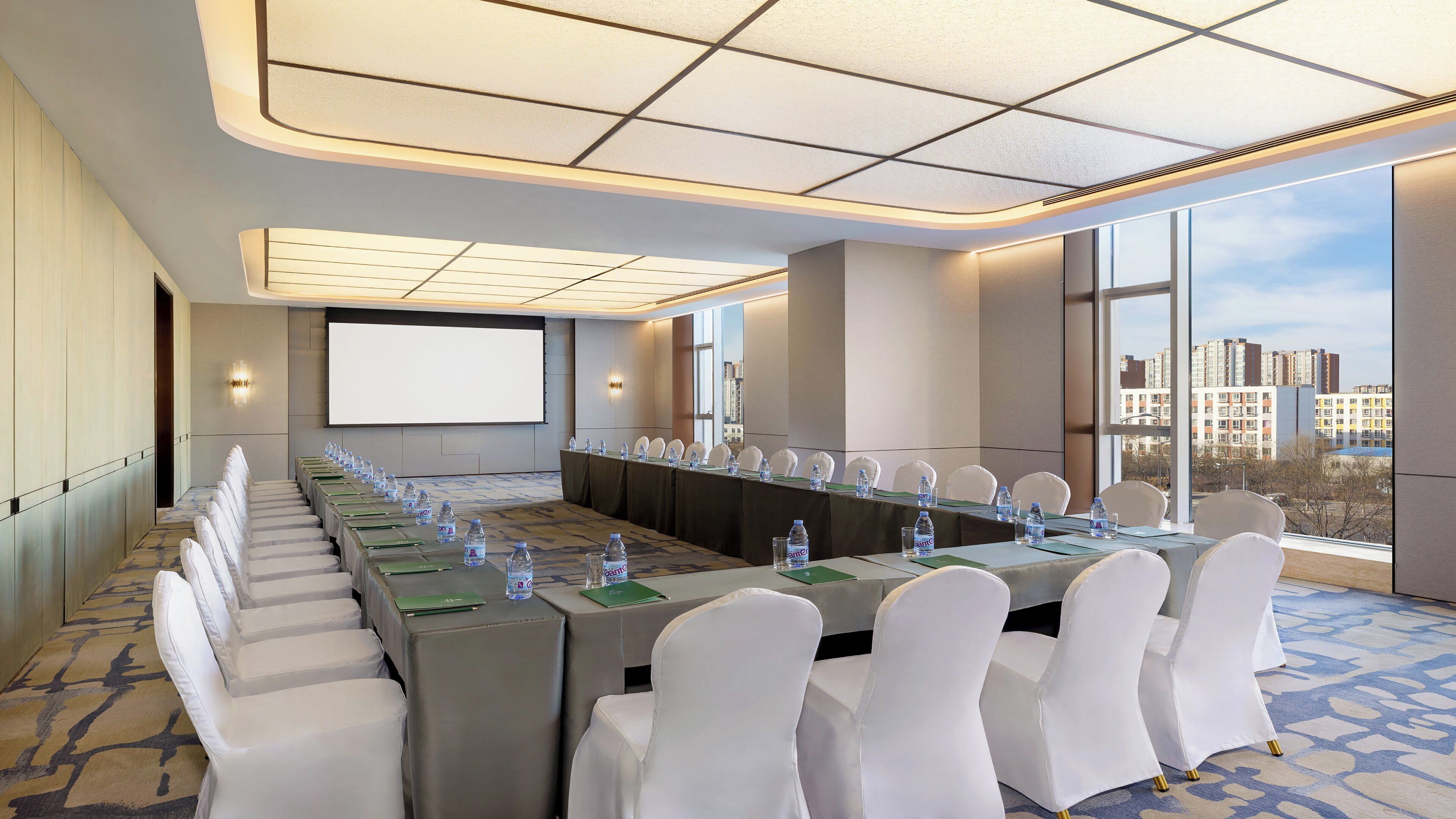 A conference room with a long table, white chairs, water bottles, and a projector screen.