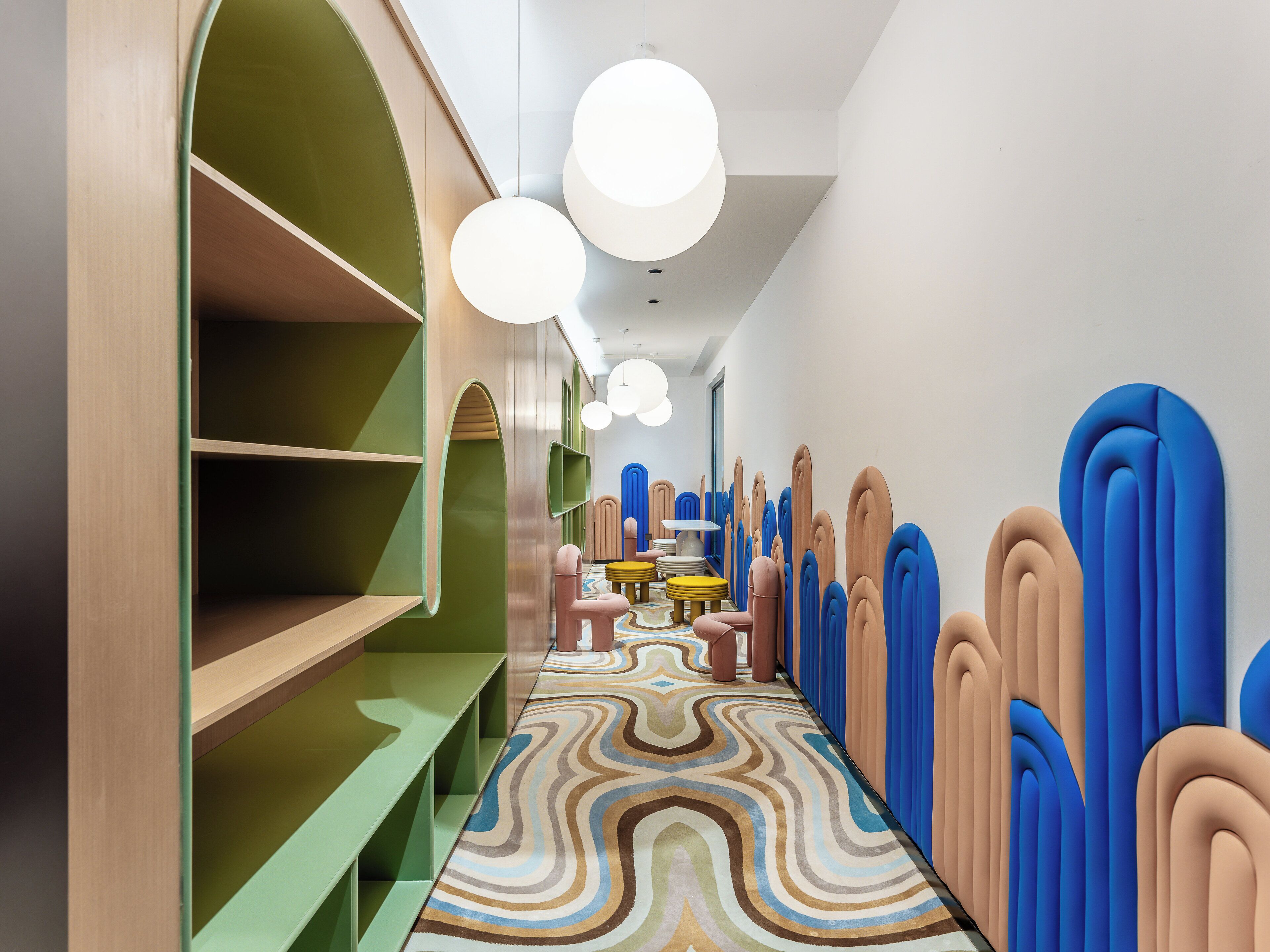 Un interior moderno con un largo pasillo, diseños de pared en tonos verdes y azules, y un suelo estampado.