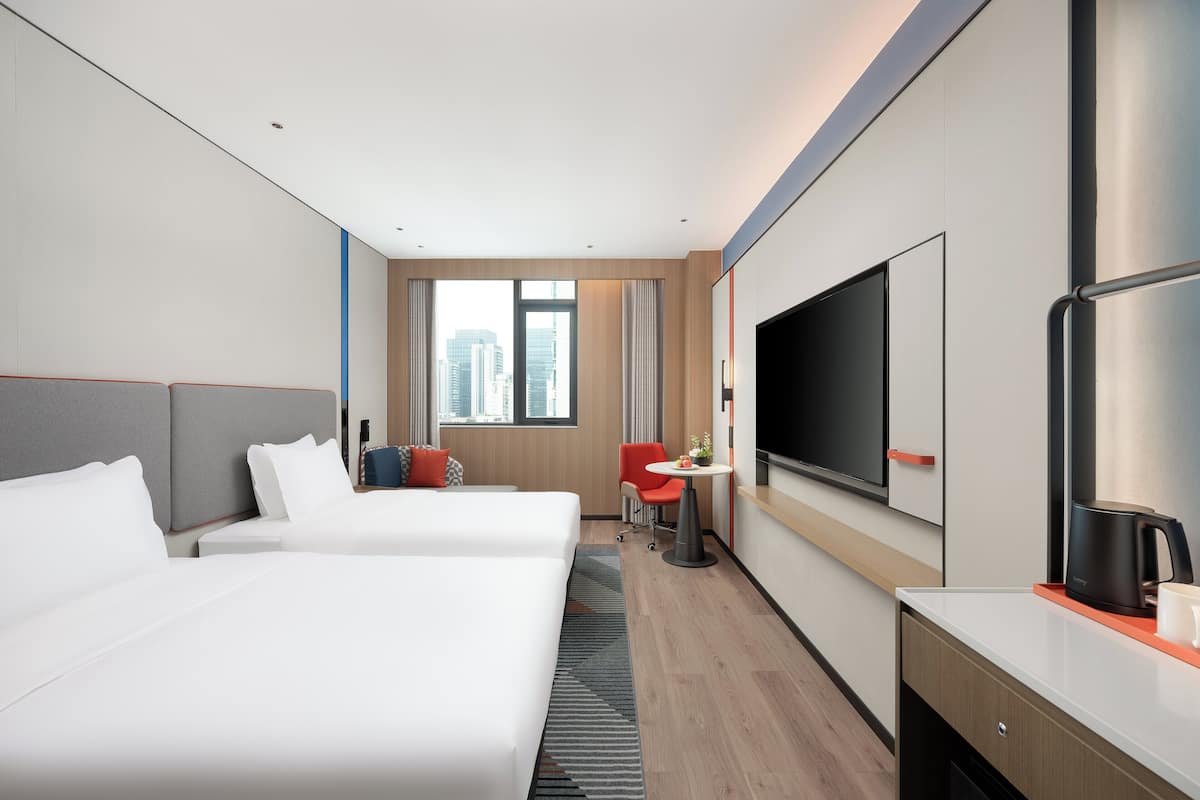 A hotel room with two beds, a desk, a TV, and a city view.