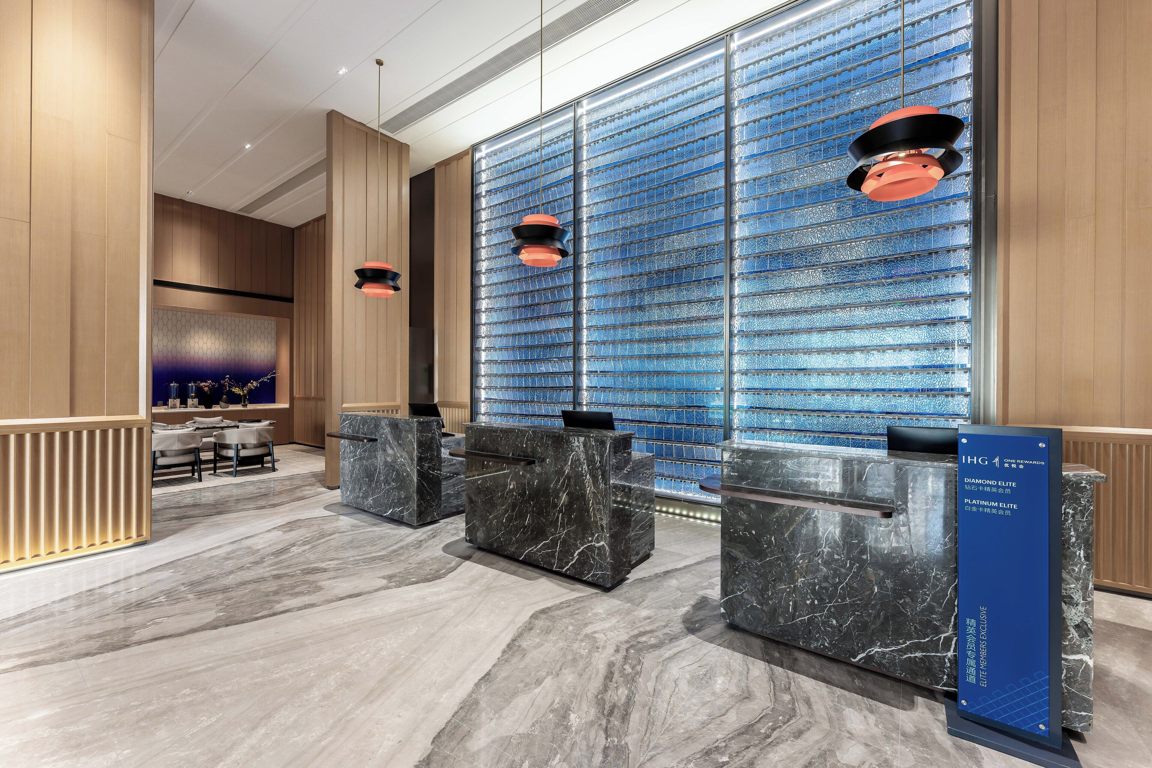 A modern reception area with marble counters, a blue patterned wall, and pendant lighting.