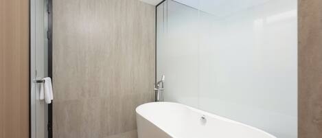 A modern bathroom with a freestanding bathtub, a glass shower enclosure, and a wooden door.