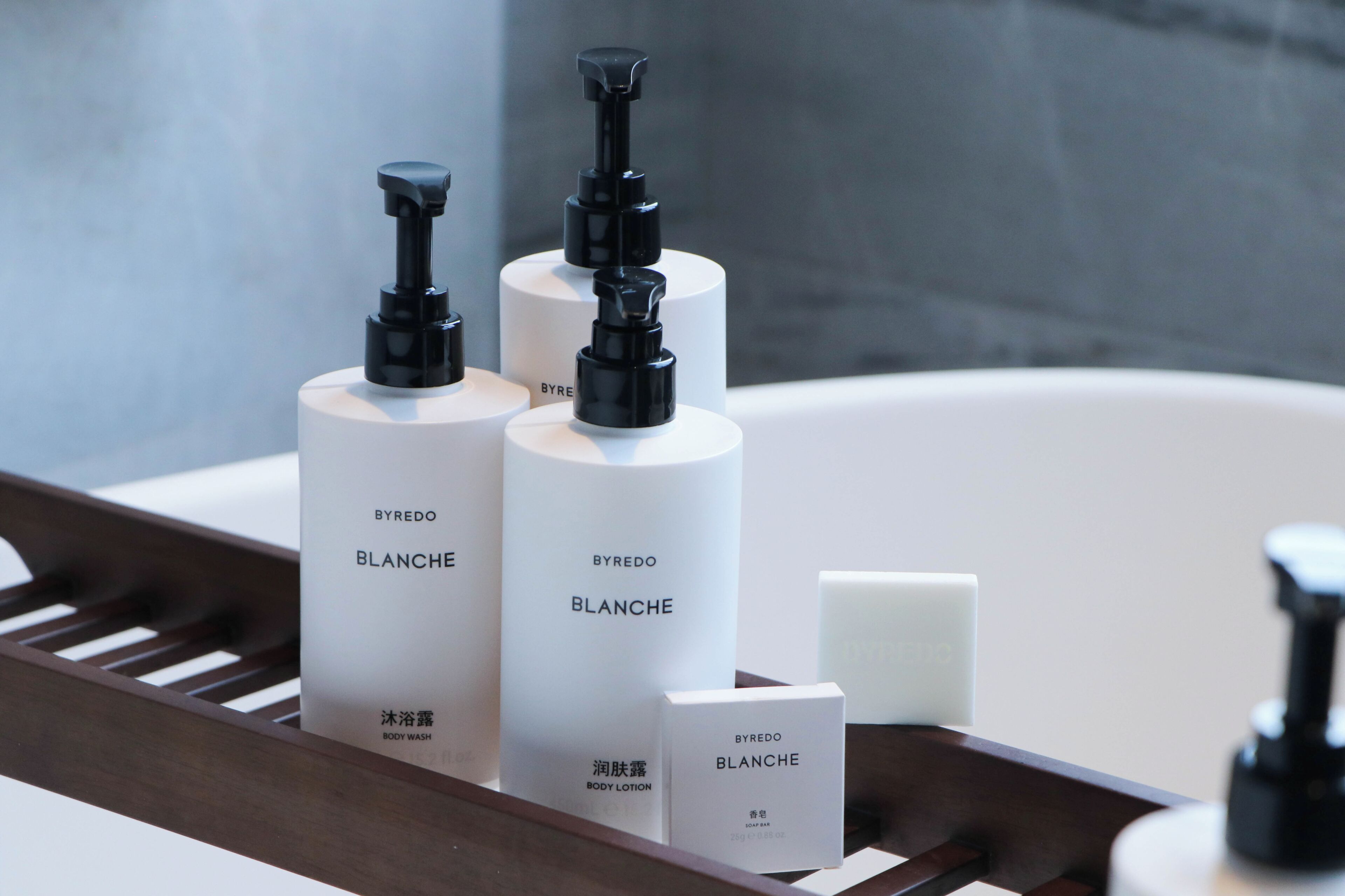 Ein Badezimmer mit einer Holztablett, auf dem sich drei Flaschen BYREDO BLANCHE Duschgel und Lotion sowie eine Seife befinden.