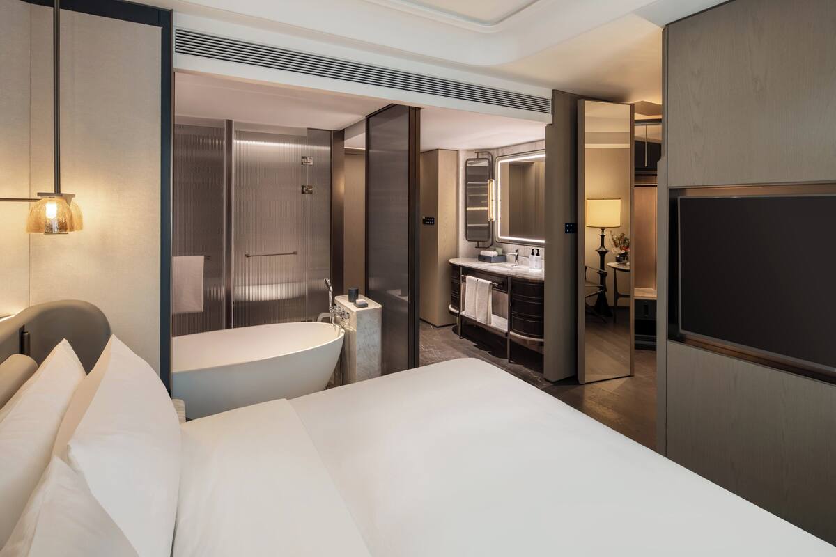 A hotel room with a large bed, a bathroom with a bathtub, a sink, and a mirror.