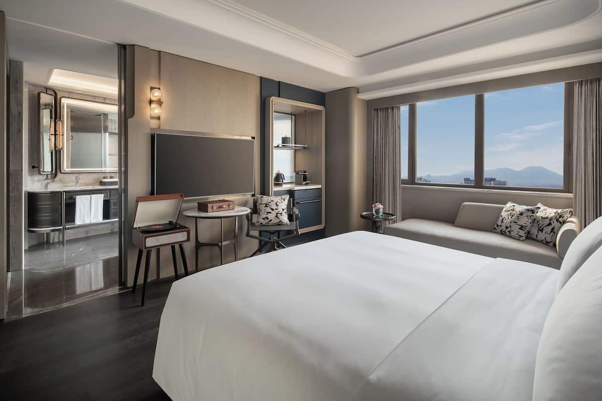 Een hotelkamer met een groot bed, een bureau met stoel, een kleine tafel, een spiegel en uitzicht op de bergen.