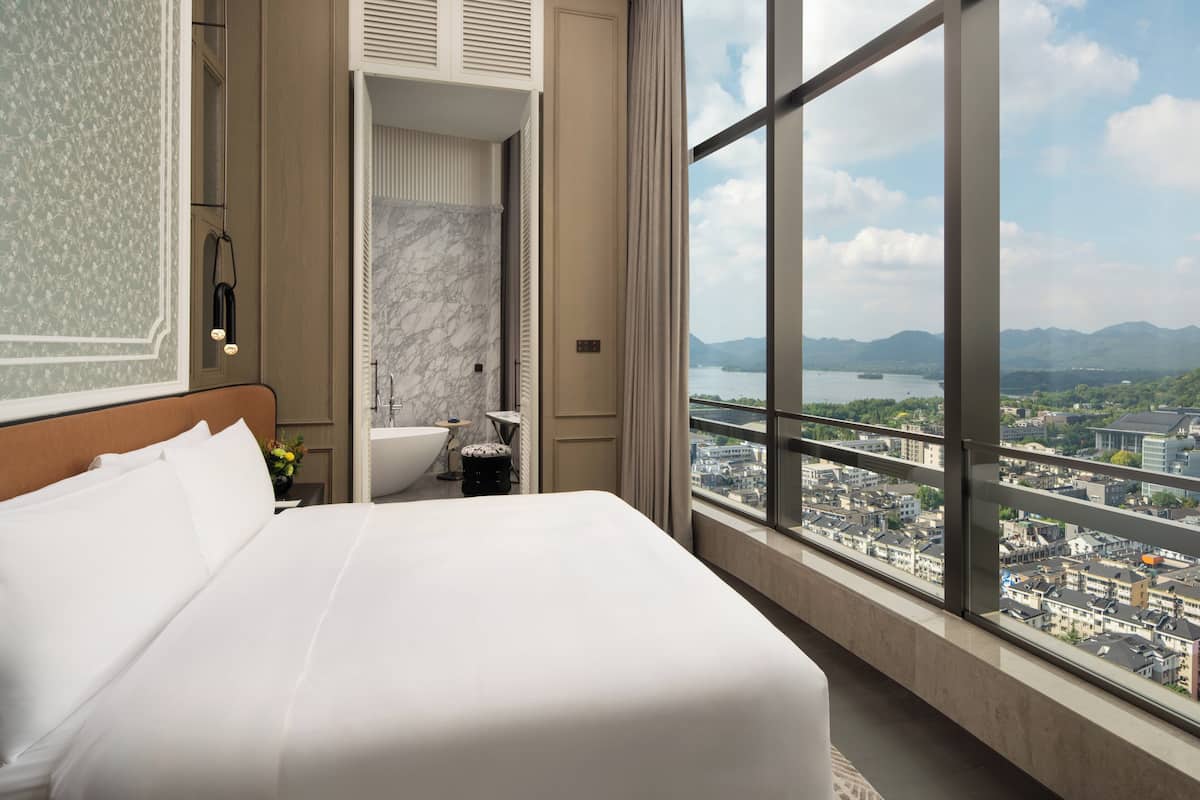 Een hotelkamer met een groot bed, een badkamer met een bad en uitzicht op de stad door grote ramen.