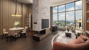 A modern living room with a marble accent wall, a flat-screen TV, a dining area with a round table and chairs, and a large window offering a city view. - Intercontinental Hangzhou Wulin by IHG (Hangzhou)