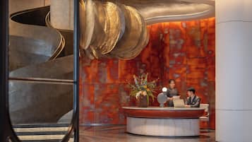 A modern reception desk with a marble top, a large vase of flowers, and a spiral staircase in the background.
